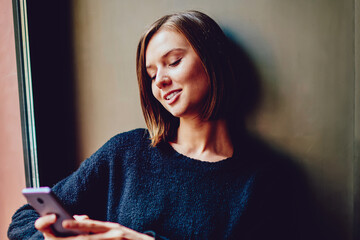 Cheerful young woman using free high speed internet connection for chatting online on smartphone...