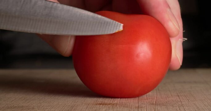Macro close-up of ripe red tomato slicing on a chopping board with knife. Cooking, food preparation, culinary