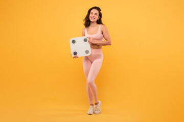 A woman wearing a pink outfit is seen holding a scale with a focused expression. The scale is being...