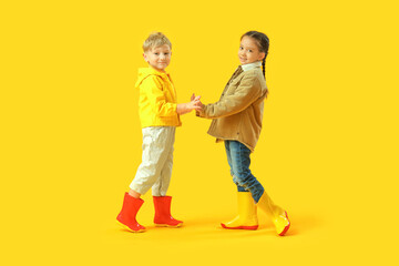 Little children in rubber boots holding hands on yellow background