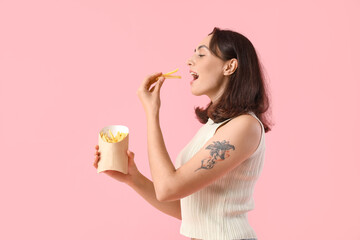 Young woman eating french fries on pink background
