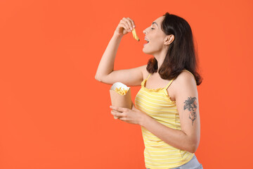 Young woman eating french fries on orange background