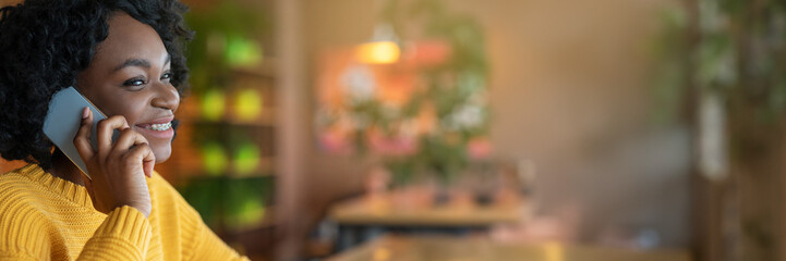Side view of young african american young woman talking by modern smartphone, cafe interior, close up, panorama with copy space