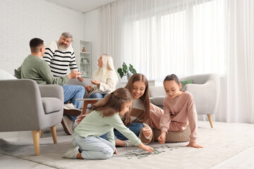 Happy mother with her little daughters doing puzzle at home