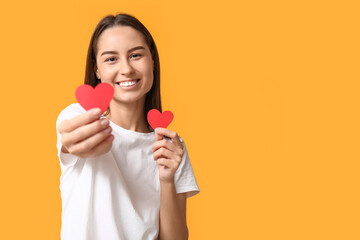Beautiful young woman with paper hearts on yellow background