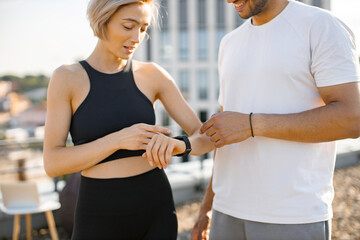 Fototapeta premium Young sports couple looks at physiological indicators of heart rate, blood pressure and pulse on smart watch after sports training. Fit happy sportsman and sportswoman monitor the health of bodies.