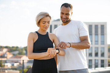 Fit happy sportsman and sportswoman monitor the health of bodies. Young sports couple looks at...