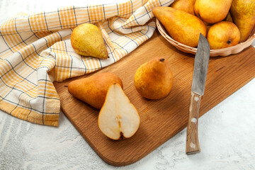 Cutting board with whole and halves pears, wicker basket and yellow kitchen towel on white wooden background..