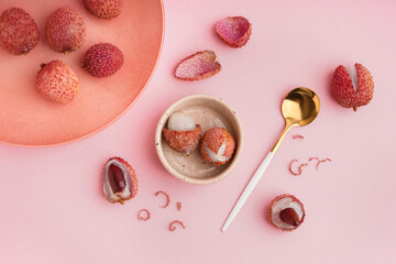 Bowl with tasty litchi fruit and spoon on pink background