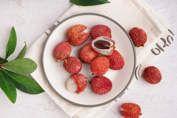 Plate with delicious litchi fruit on light background