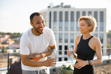 Young couple having fun laughing after morning workout on the roof of the house. Athletic man in...