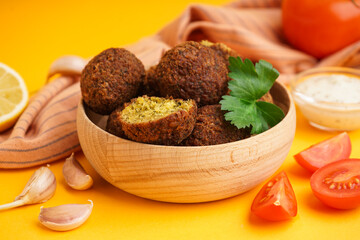 Wooden bowl with delicious falafel balls, tomatoes and garlic on orange background, closeup