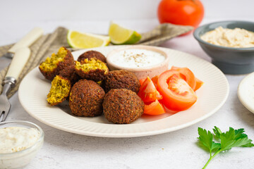 Plate with delicious falafel balls, sauce and tomatoes on light background, closeup