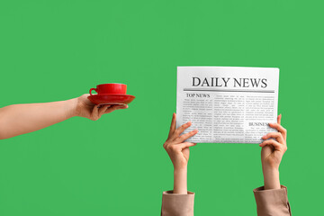 Female hands with newspaper and cup of coffee on green background