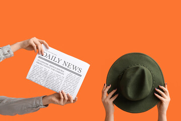 Female hands with newspaper and hat on orange background