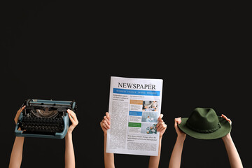 Female hands with newspaper, hat and vintage typewriter on black background