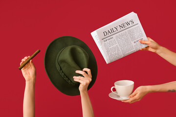 Female hands holding newspaper with cup of coffee, hat and cigar on red background