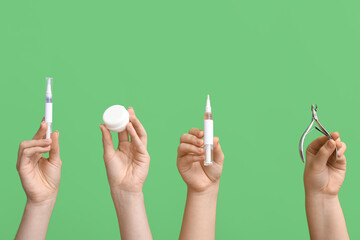 Female hands holding cuticle oil pens with nail cutter and jar of cream on green background