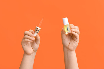 Female hands with bottle of cuticle oil and pipette on orange background