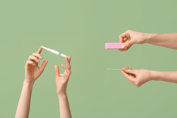 Female hands with cuticle oil pen, orange stick and nail buffer on green background