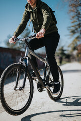 Obraz premium A young adult male rides his mountain bike along a park path, enjoying the warm sunshine and outdoor activity while dressed in casual attire.