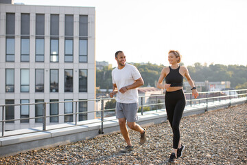 Young sports couple doing sports in morning on roof of modern building. Happy man and woman jogging...