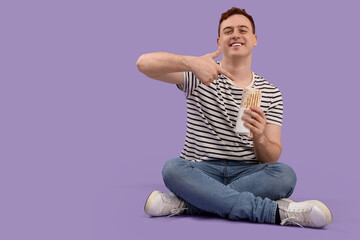 Young man sitting and holding doner kebab on purple background