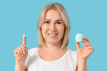 Beautiful mature happy woman with jar of face cream on blue background