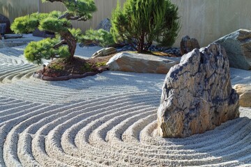 Zen garden with raked sand, stones, and miniature bonsai trees in sunlight.