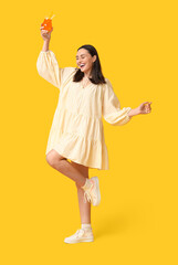 Beautiful young woman with glass of cocktail on yellow background. Summer party