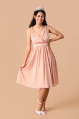 Fototapeta premium Happy young African-American woman in stylish prom dress and tiara on brown background