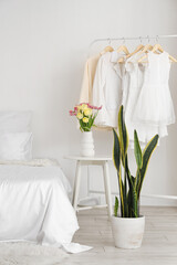 Interior of light bedroom with clothes rack and tulips in vase