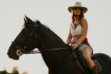 Low angle view of cowgirl with cowboy hat horseback riding at ranch.