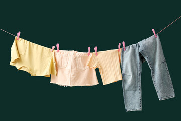 Different clean clothes hanging on rope against green background