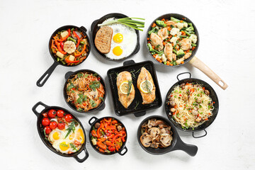 Frying pans with different tasty dishes on light background
