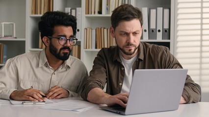 Two diverse anxious displeased businessmen Arabian Indian Caucasian men male colleagues coworkers develop business project online together brainstorming working on laptop upset with mistake in office