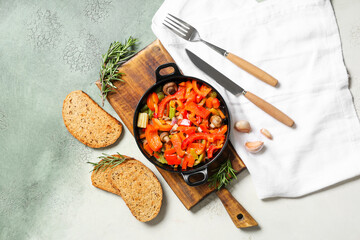 Frying pan with tasty vegetables, bread and cutlery on grunge background