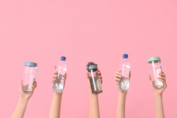 Female hands with different bottles of water on pink background