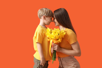 Happy woman and her little son with bouquet of beautiful narcissus on orange background