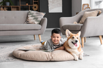 Little happy Asian boy reading book with cute Corgi dog at home