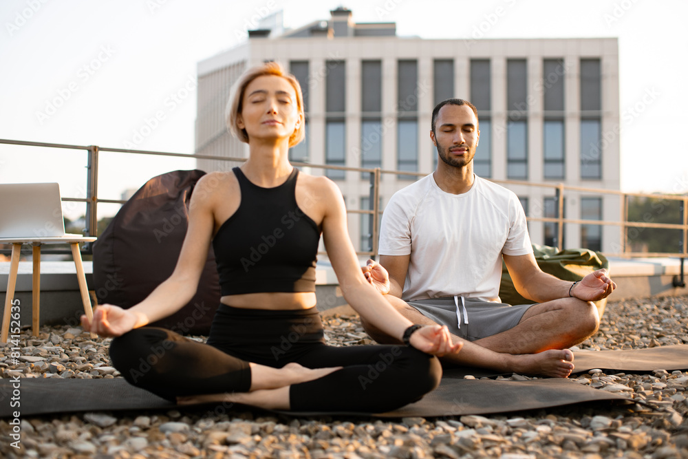 Wall mural athletic man and flexible woman meditating in morning on urban background. young couple in sportswea