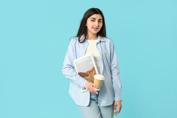 Fototapeta premium Beautiful young happy woman with magazine and cup of coffee on blue background