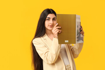 Beautiful young woman reading magazine on yellow background