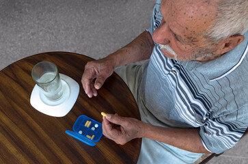 Hombre mayor, en edad avanzada, tomando una píldora de su pastillero o estuche de pastillas con...