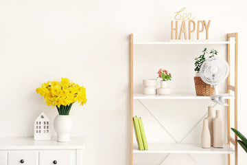 Modern electric fan with beautiful daffodils on shelving unit at home