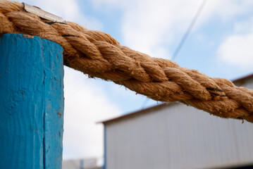 A rope is tied to a blue pole. The rope is brown and has a lot of knots. The rope is tied to the...