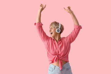 Mature woman in headphones listening to music on pink background