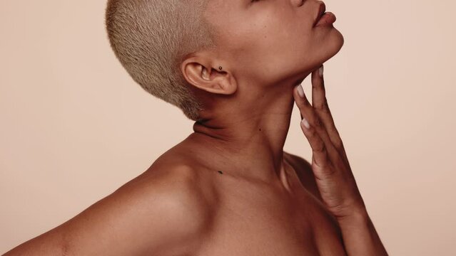 Profile of a serene woman with a short hairstyle, hand gently touching her face against a neutral background.