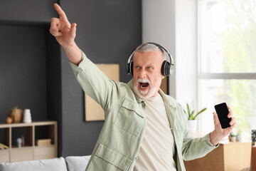 Mature man in headphones with mobile phone listening to music at home