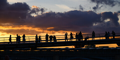 Silhouettes of people on Millennium Bridge watching orange sunset with no recognizable people